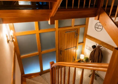 Eingangsbereich mit Holztreppe, großer Holztür und warmem Licht im Refugium am Ursprung